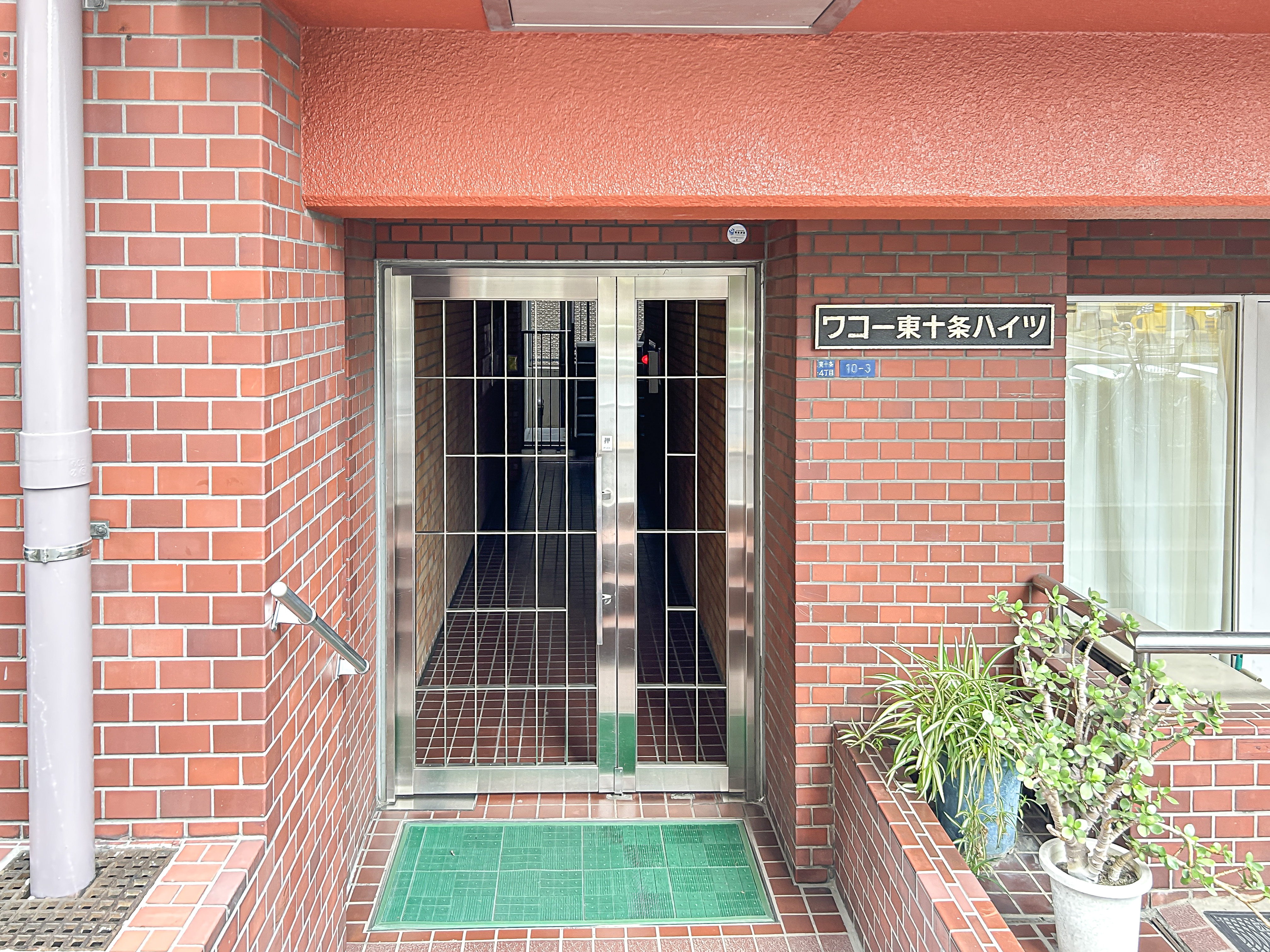 建物の入口部分（金属製ゲート、マット、周辺壁面）が主体の画像